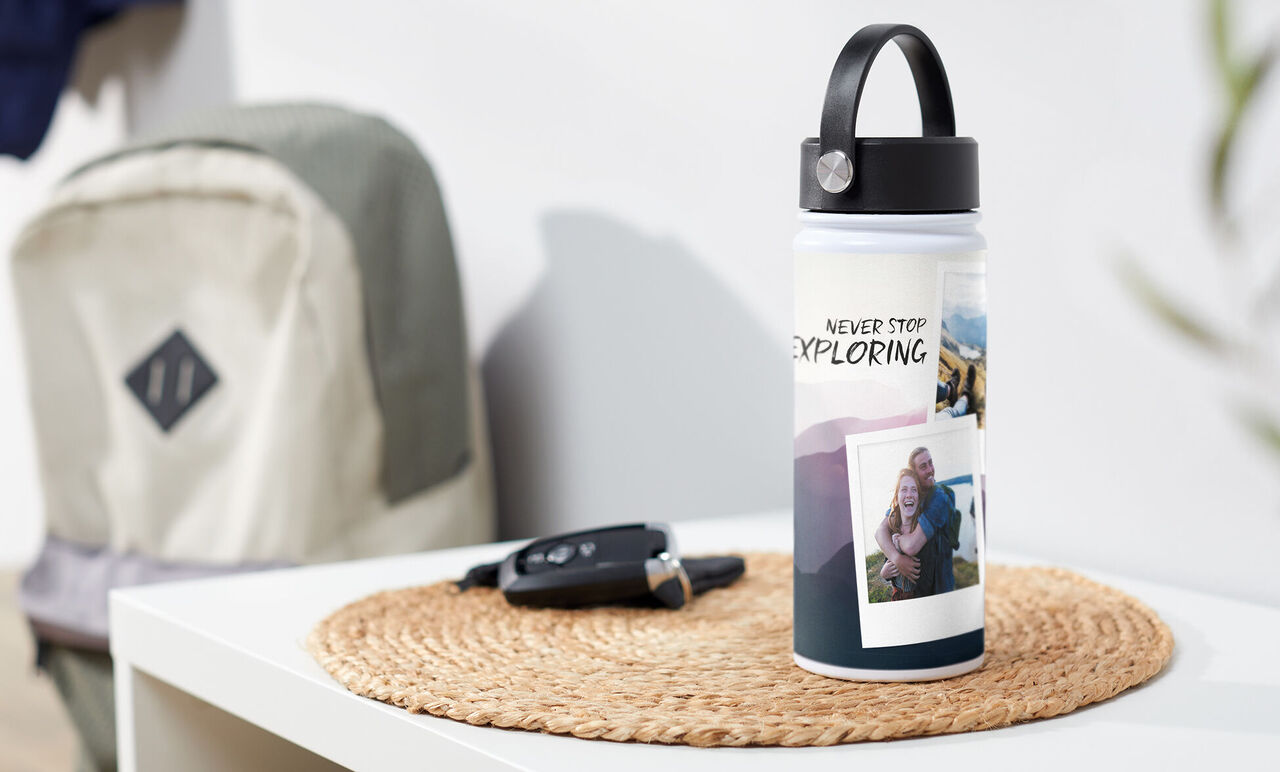 Waterfles met tekst 'Never Stop Exploring' en foto's op een tafel. Achtergrond heeft rugzak en autosleutel