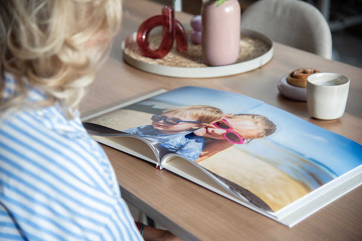 Een gelukkige vrouw bekijkt een CEWE fotoboek met vakantiekiekjes van haar en een kind op het strand