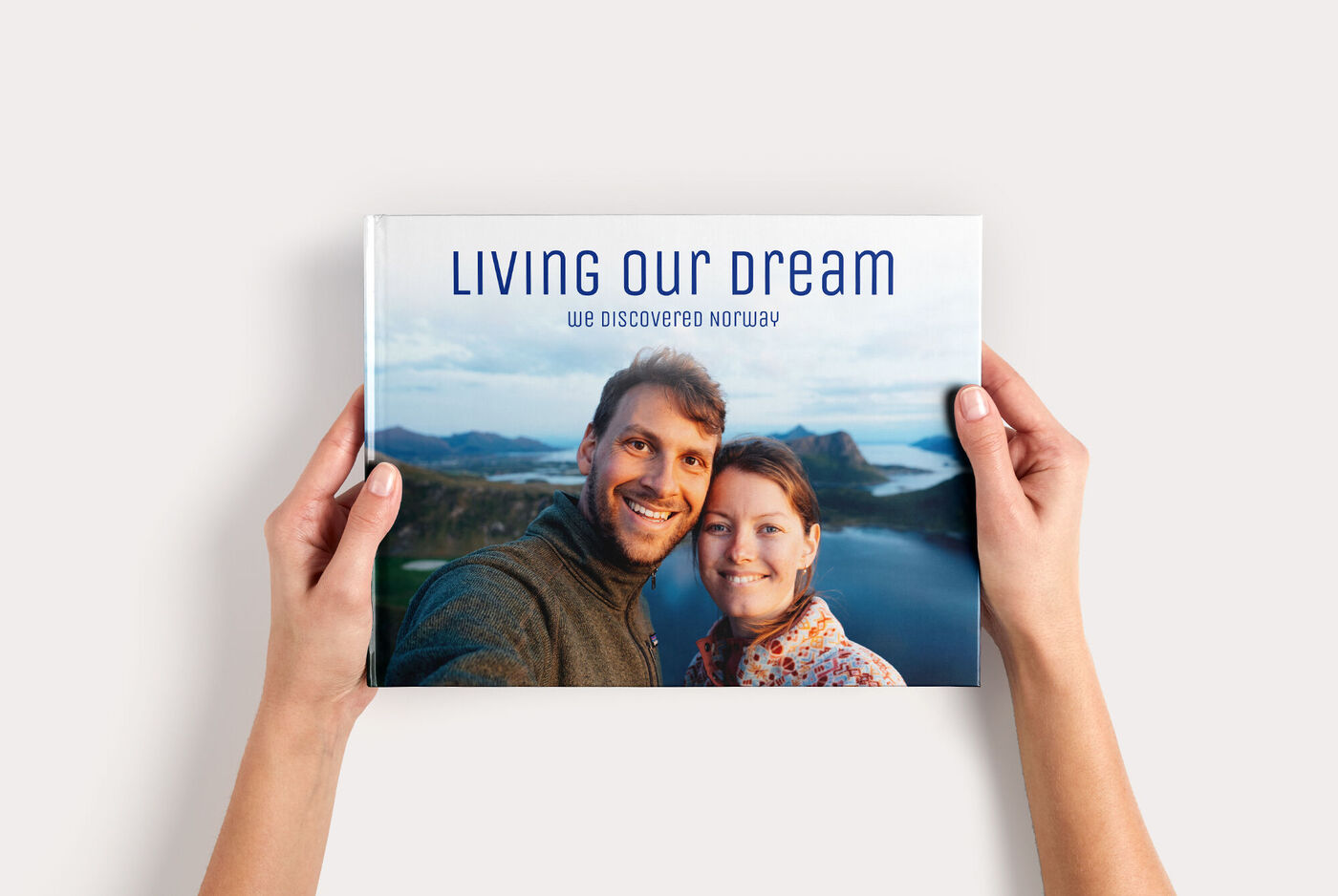 Fotoboek Large Liggend met een selfie van een stel voor een meer en de titel “Living our dream”, vastgehouden door twee handen.