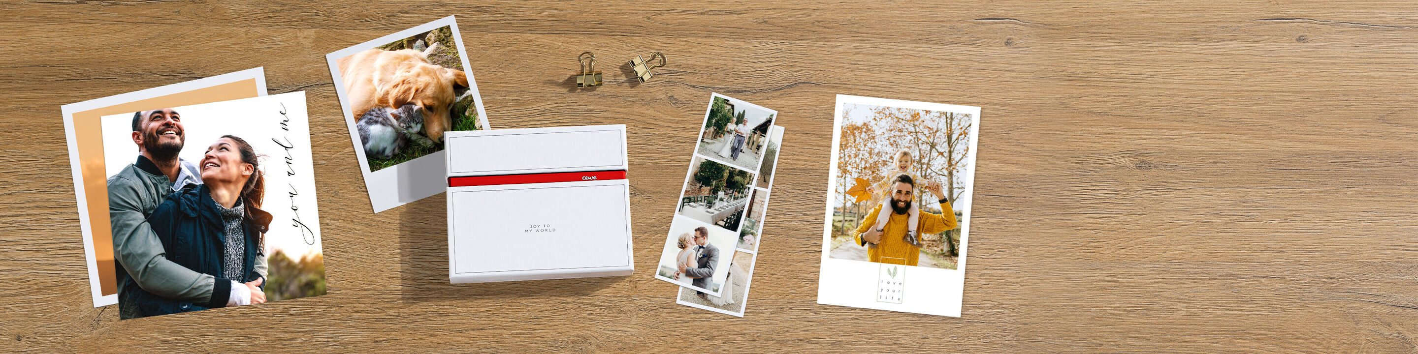 Vier persoonlijke fotoafdrukken liggen op een houten tafel, omringd door kleine clips. De foto's tonen gelukkige momenten van twee personen. Een CEWE Fotokalender ligt in het midden.