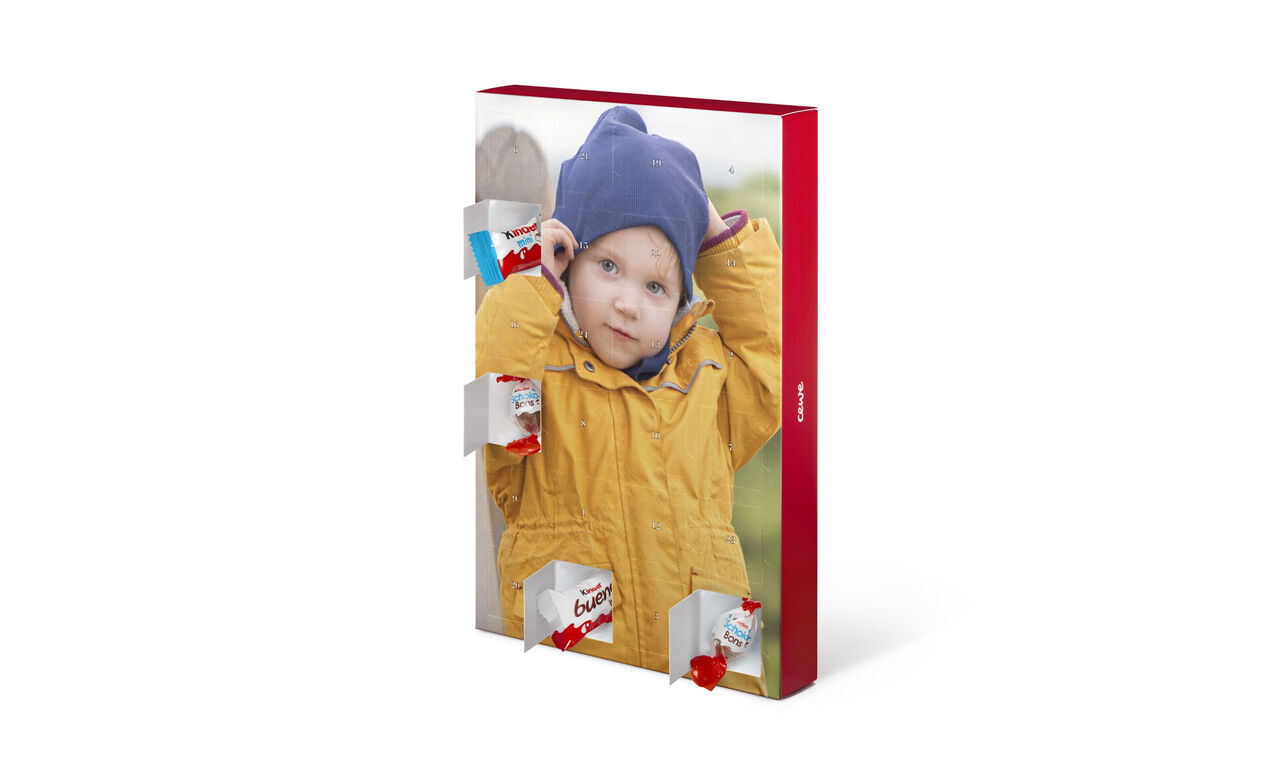 Een kind in gele regenjas staat vrolijk voor een grote rode muur met vakjes voor verrassingen. Het pakt een lekkernij.