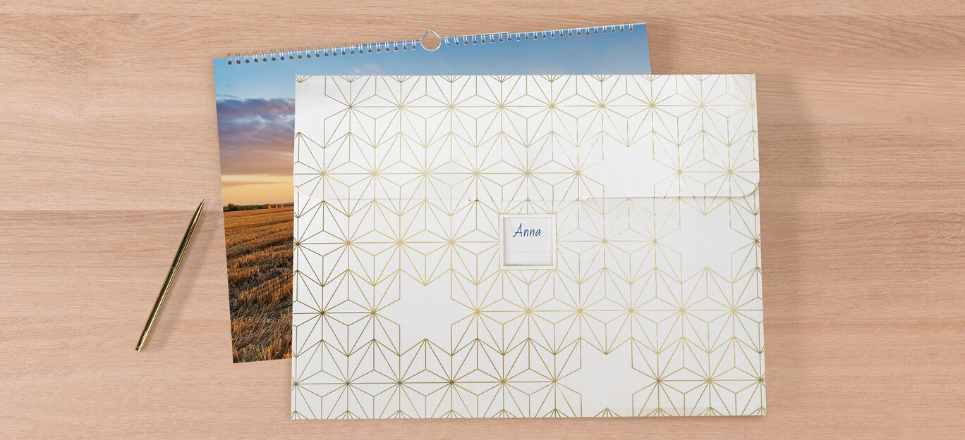 Een decoratieve envelop met gouden geometrische patronen naast een kalender met een landschap.