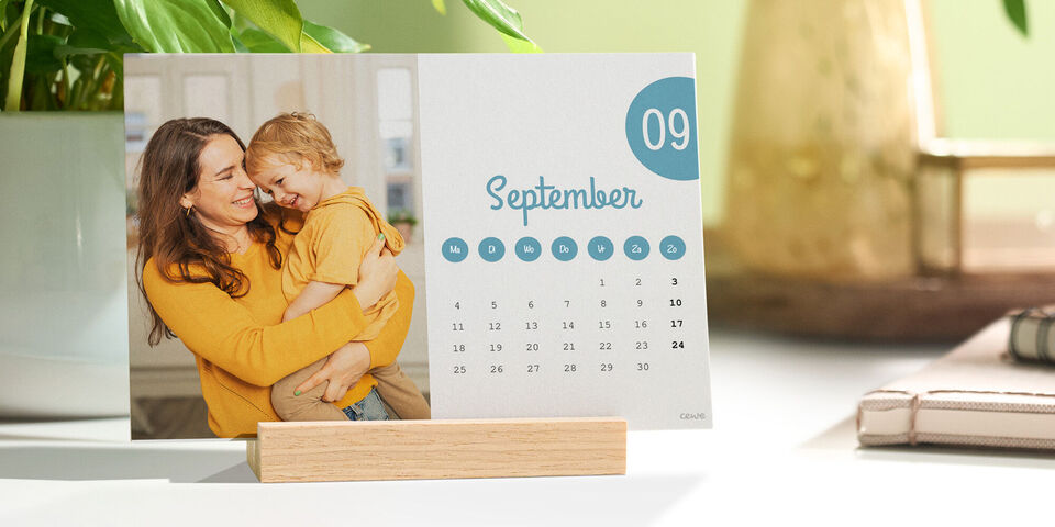 Een bureaukalender met een foto van moeder met kind staat op een bureau in een houten standaard.