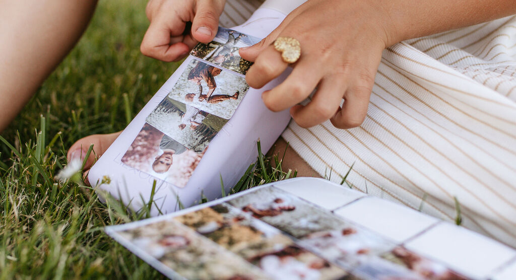 Iemand bekijkt foto's in een CEWE fotoboek met een losse foto in de hand, omgeven door groen gras.