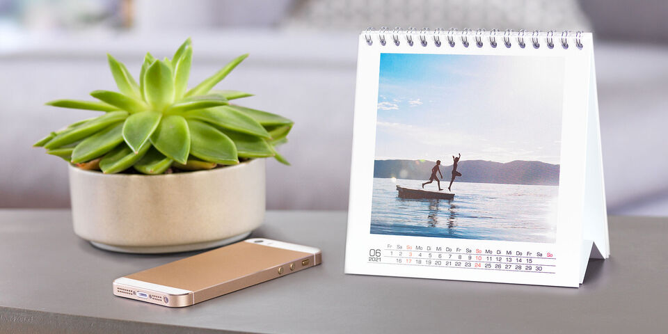 Een vrolijk moment, twee mensen dansen op een boot op het water, met een kalender en een plant op de voorgrond.