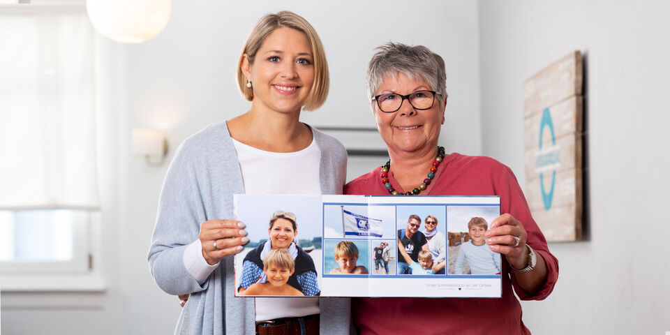 Twee vrouwen houden een geopend fotoboek met familiefoto's vast.