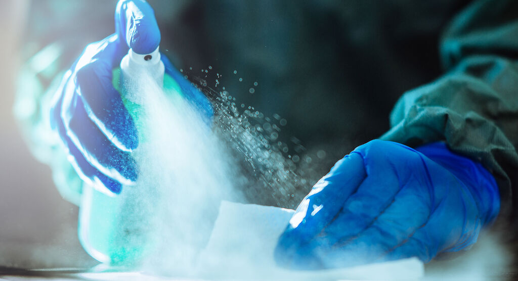 Een persoon met blauwe handschoenen spuit reinigingsmiddel op een wit oppervlak.