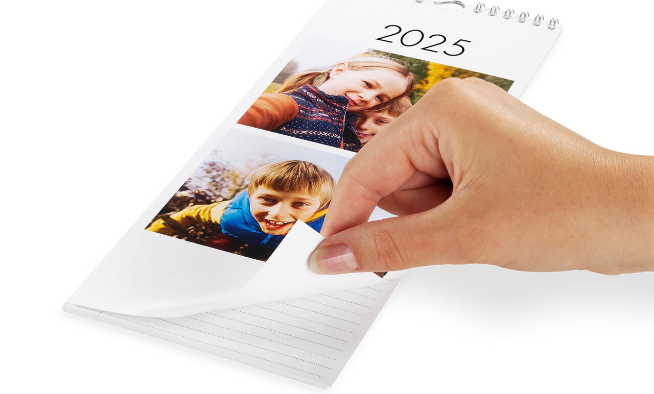 Een hand bladert door een CEWE Fotokalender 2025 met foto's van gelukkige momenten.