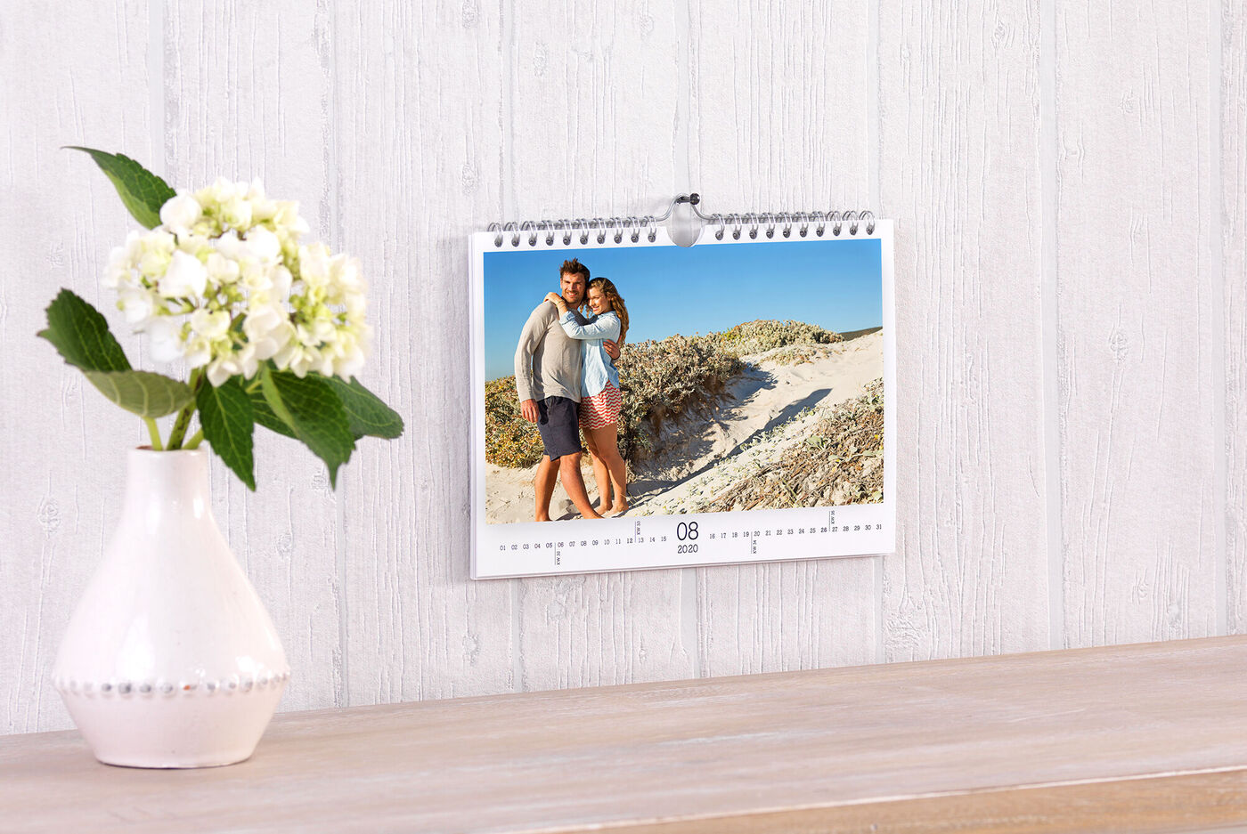 Een kalender hangt aan de muur. Op de foto een paar dat elkaar omhelst, met een zandstrand op de achtergrond.