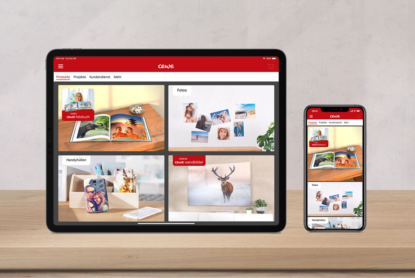 Een tablet en smartphone tonen CEWE-producten zoals fotoboeken en wenskaarten op een tafel.