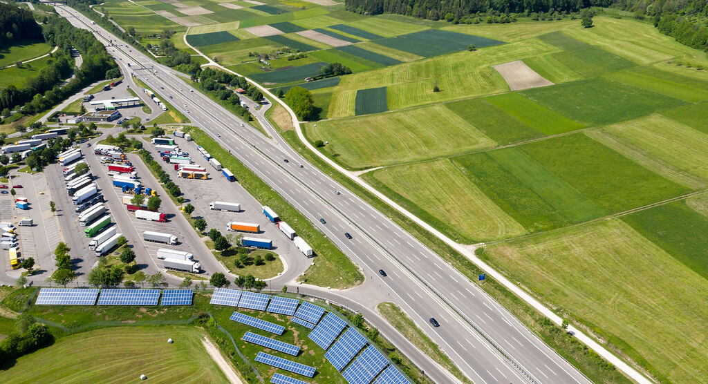 Luchtfoto van een snelweg met landbouwvelden en vrachtwagenparkeerplaats.
