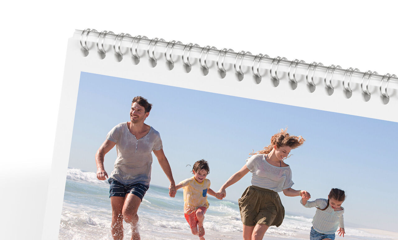 Gezin wandelt vrolijk langs het strand en geniet van de zon. CEWE-fotokalender.