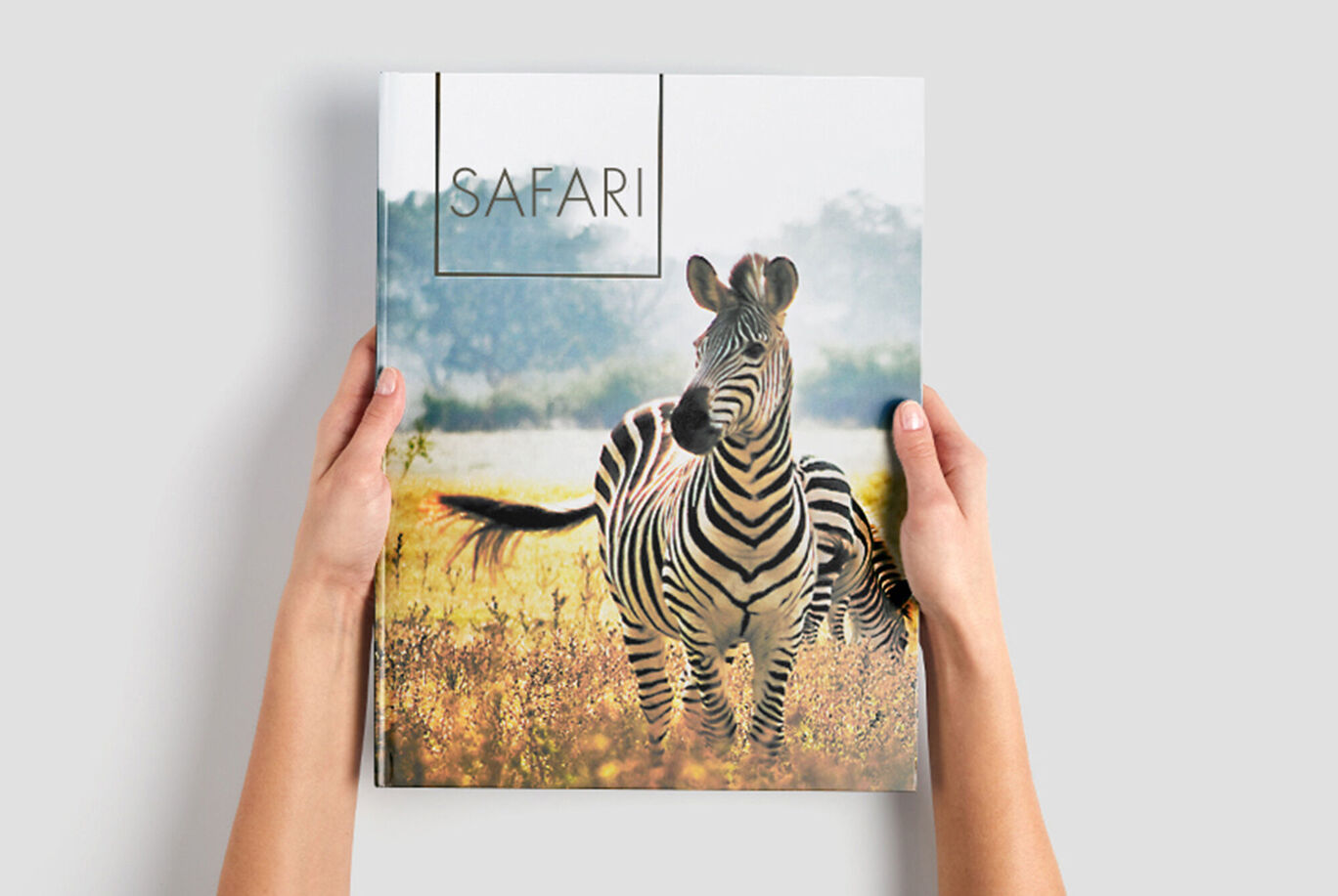 Handen houden een CEWE Fotoboek met de titel 'Safari', waarop een zebra staat.