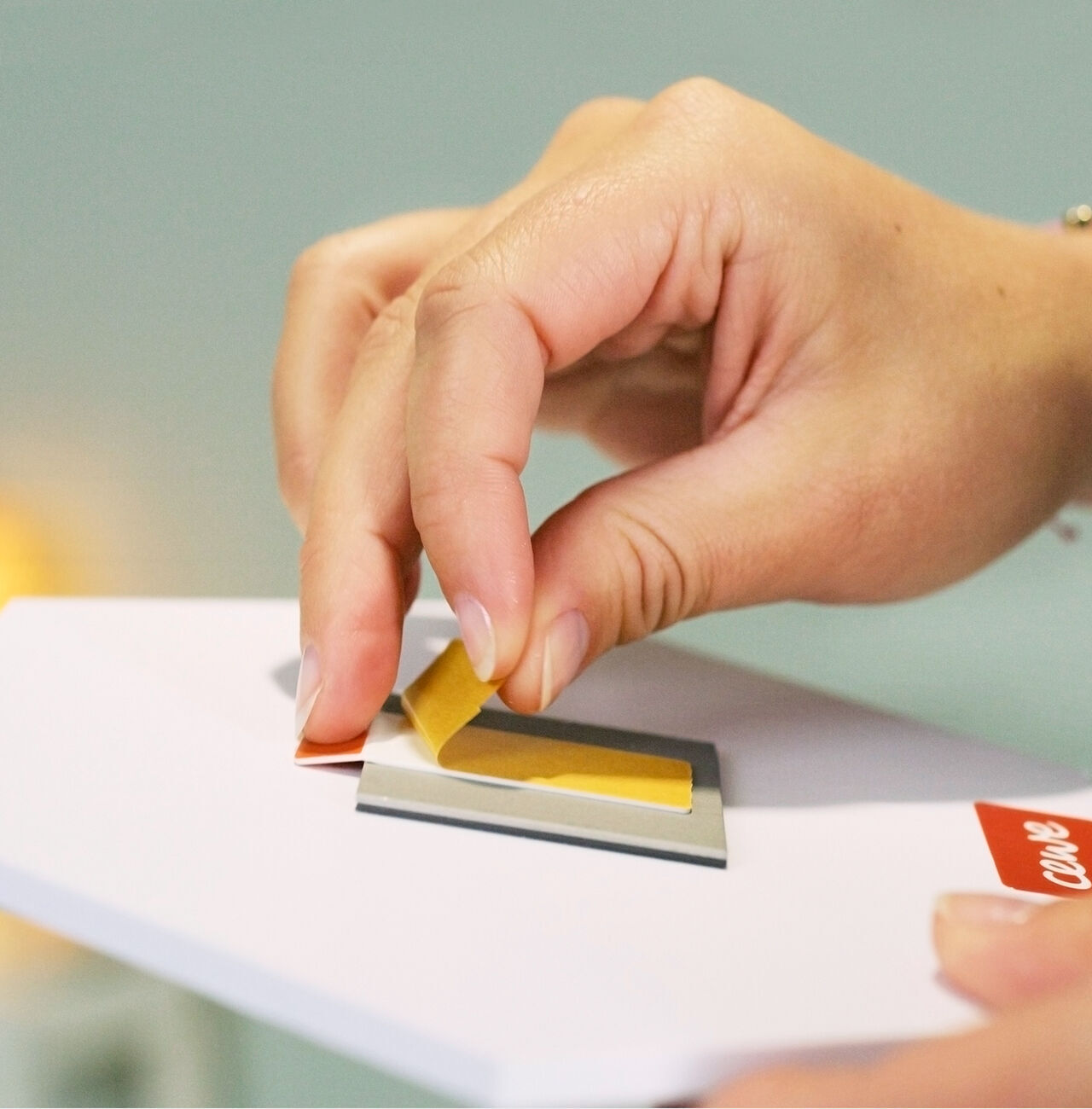 Een hand plakt een geel stuk papier op een wenskaart