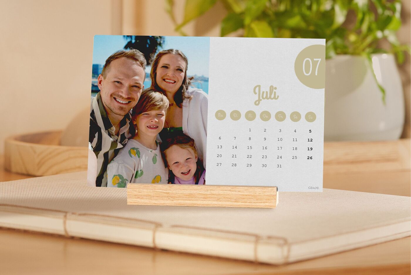 Er staat een bureaukalender op de maand juli op tafel met een vakantiefoto van een lachend gezin.