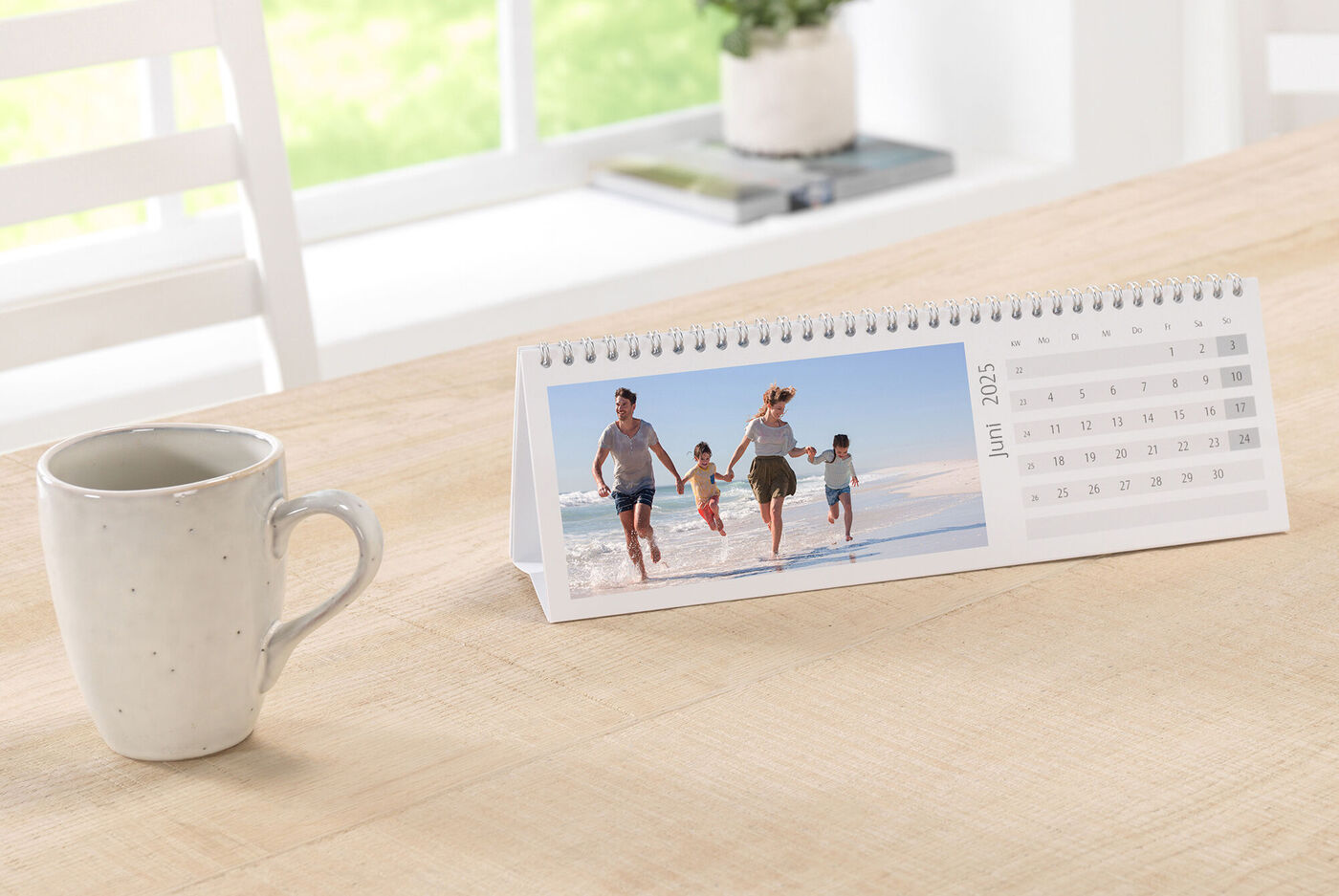Een CEWE fotokalender op tafel toont een vrolijke familie die langs het strand loopt