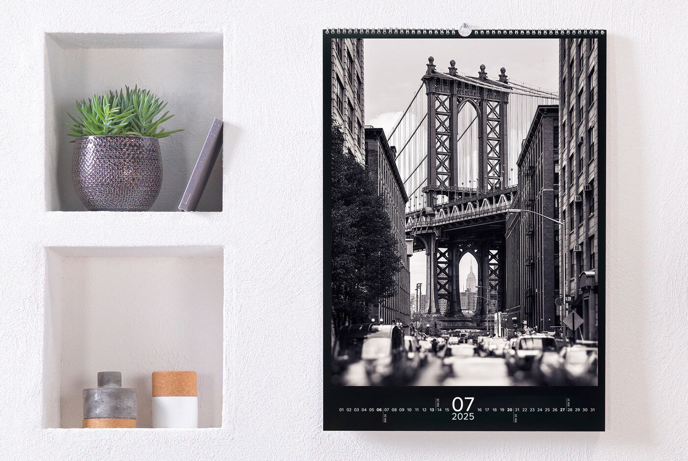 Een stijlvolle fotokalender hangt aan de muur. Juli 2025 is zichtbaar met een zwart-witfoto van de Brooklyn Bridge.
