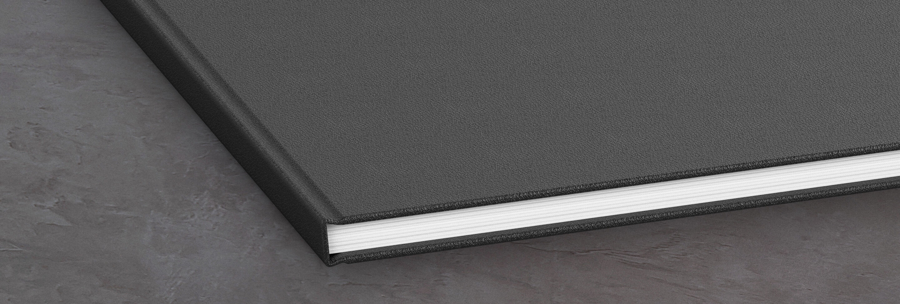 Een gesloten, zwart fotoboek ligt op een grijze ondergrond