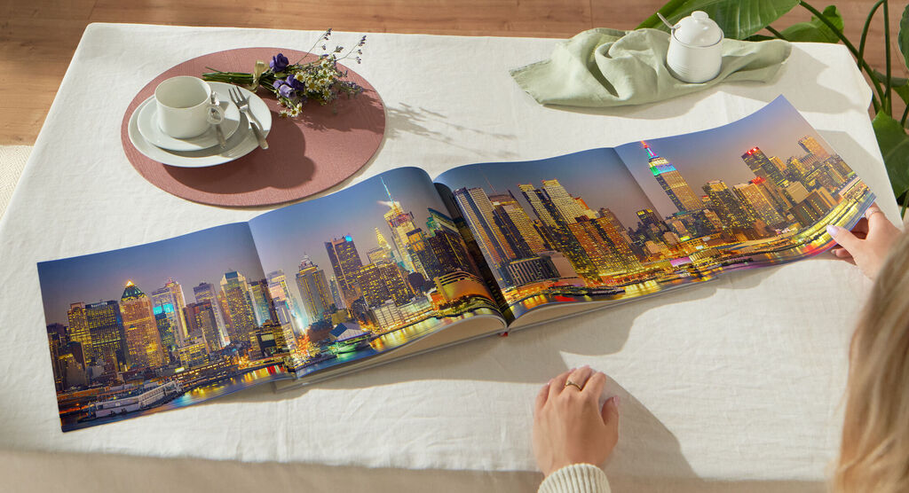 Iemand bladert door een geopend fotoboek met een stadsbeeld van Philadelphia bij nacht op een tafel.