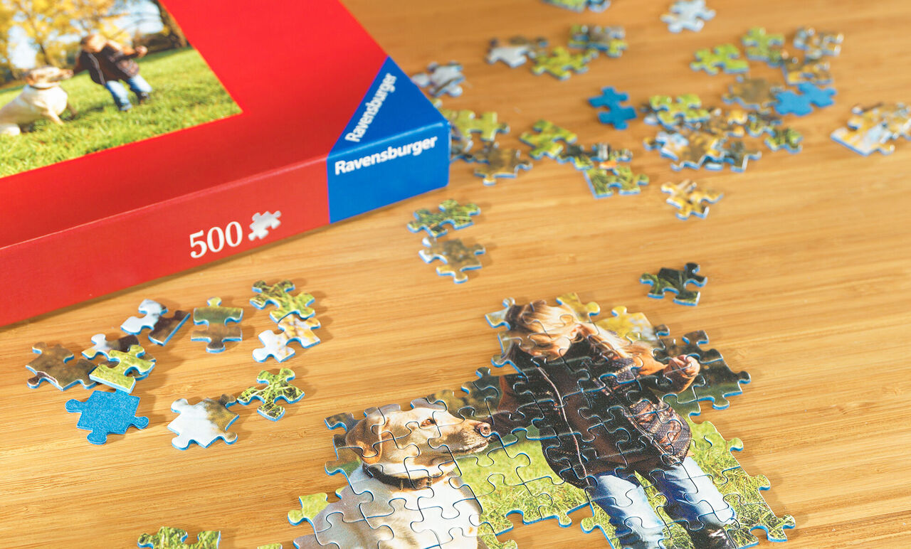Un puzzle avec une image de deux enfants et un chien. Des pièces sont éparpillées sur une table. La boîte est rouge et montre l'image en grand.