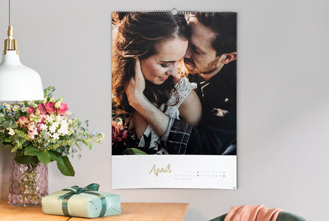 Une page de calendrier pour avril avec une image romantique de deux personnes qui s'embrassent. Le calendrier est suspendu à un mur, à côté se trouvent un cadeau joliment emballé et un vase avec des fleurs.