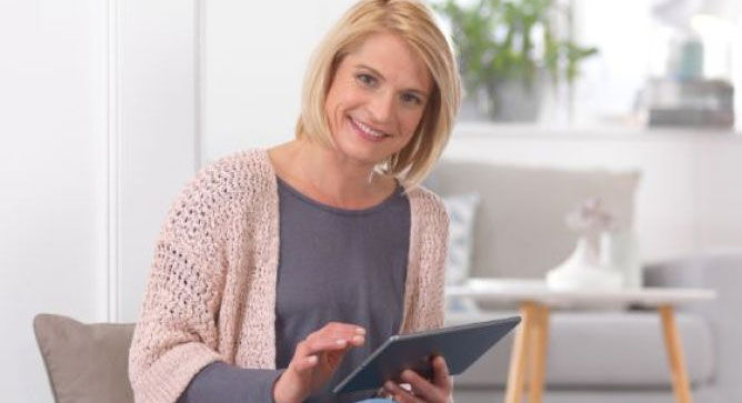 Une personne tenant une tablette, assise dans une pièce lumineuse, défile joyeusement dans le contenu.