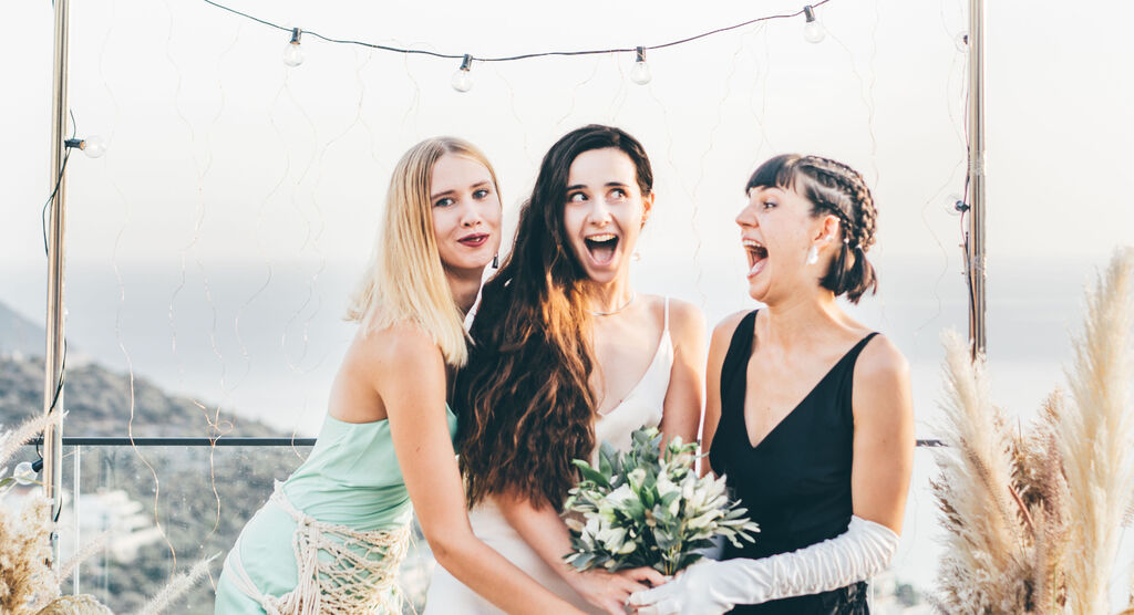 Trois femmes en tenue de fête s'enlacent affectueusement avec un bouquet de mariage.