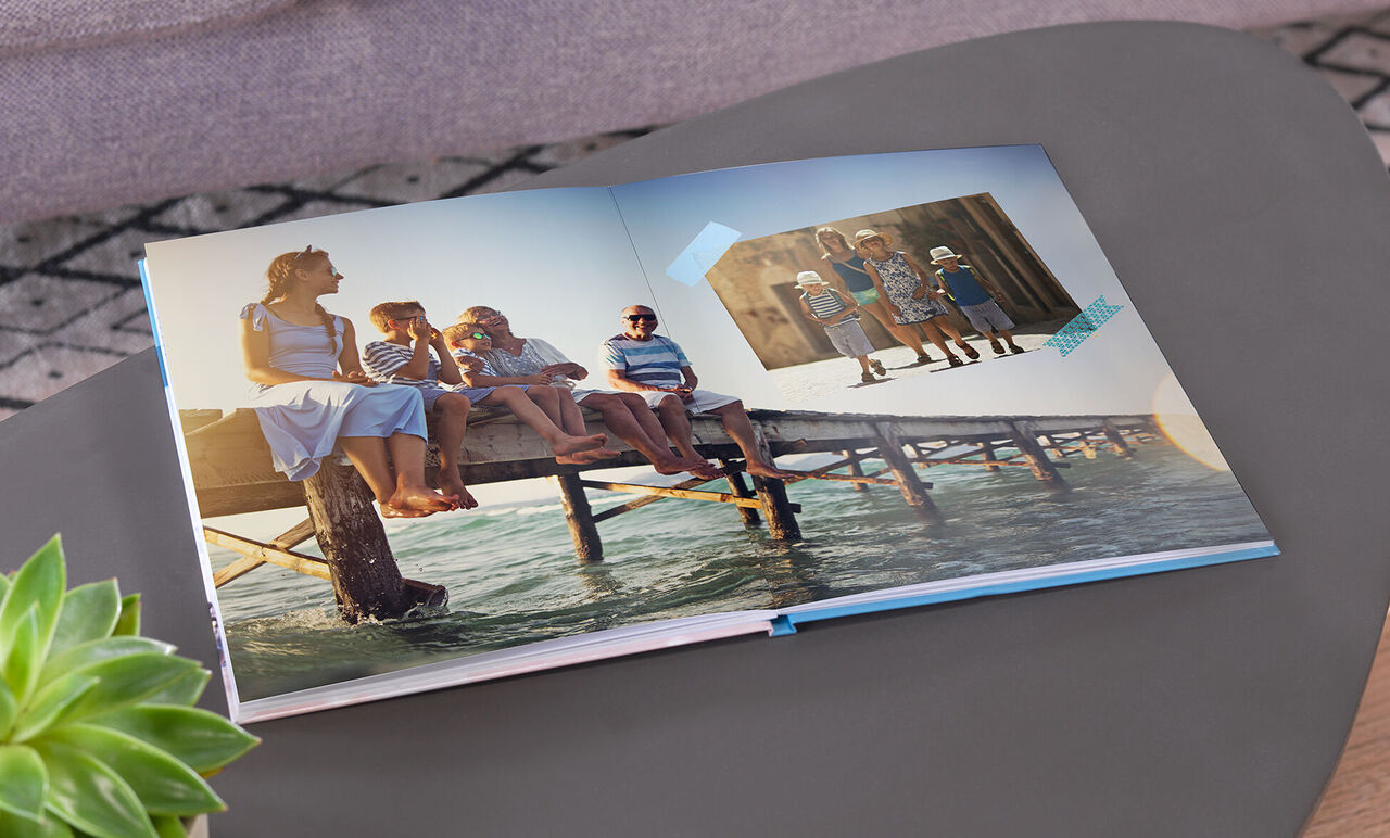 Un CEWE PHOTOBOOK ouvert est sur une table. Les pages montrent des moments familiaux à la plage avec enfants et adultes.