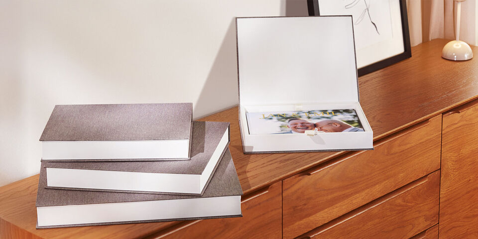 Différents albums CEWE empilés sur une commode en bois, un est ouvert avec des photos.