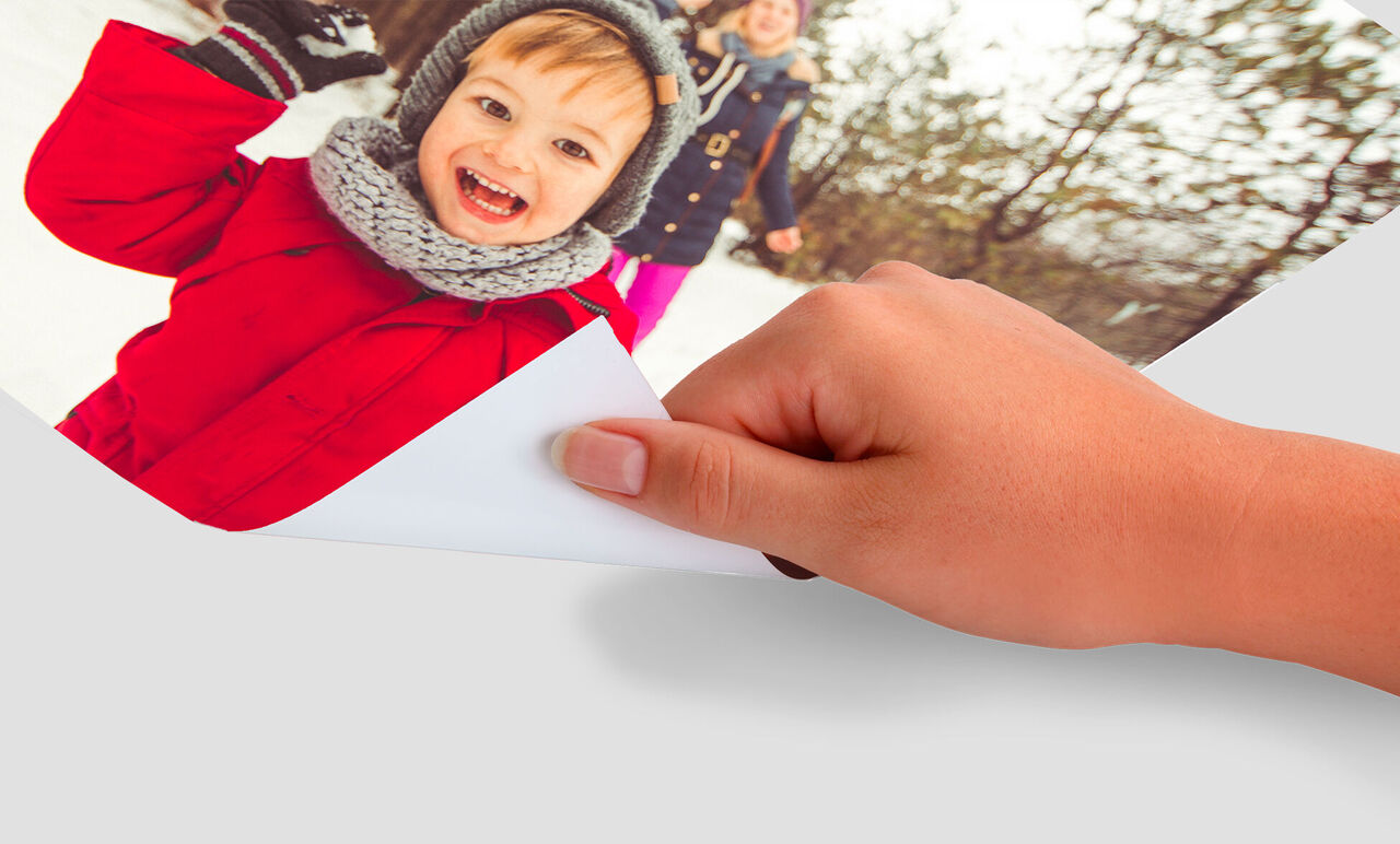 Une main tient un album photo avec un enfant joyeux et un adulte dans la neige, émettant de la joie.