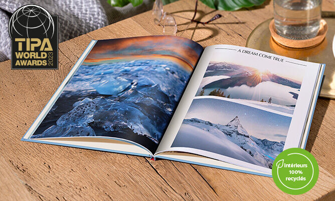 Un CEWE FOTOBUCH ouvert avec photos de paysages enneigés et un coucher de soleil.