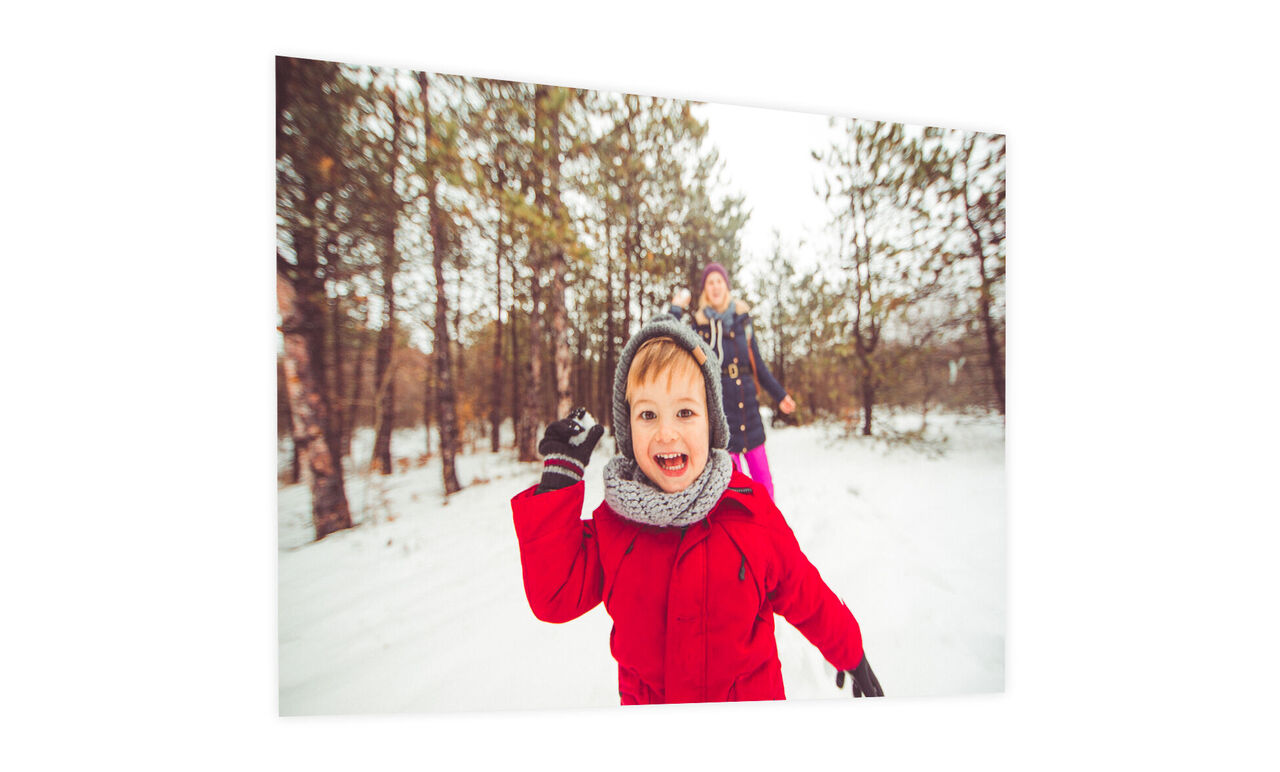 Un enfant en combinaison d'hiver rouge montre joyeusement son pouce en jouant dans la neige.