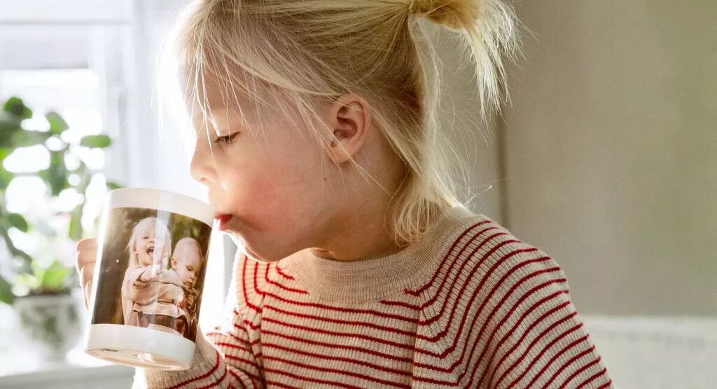 Un enfant à table tenant une tasse avec photo, entouré de plantes.