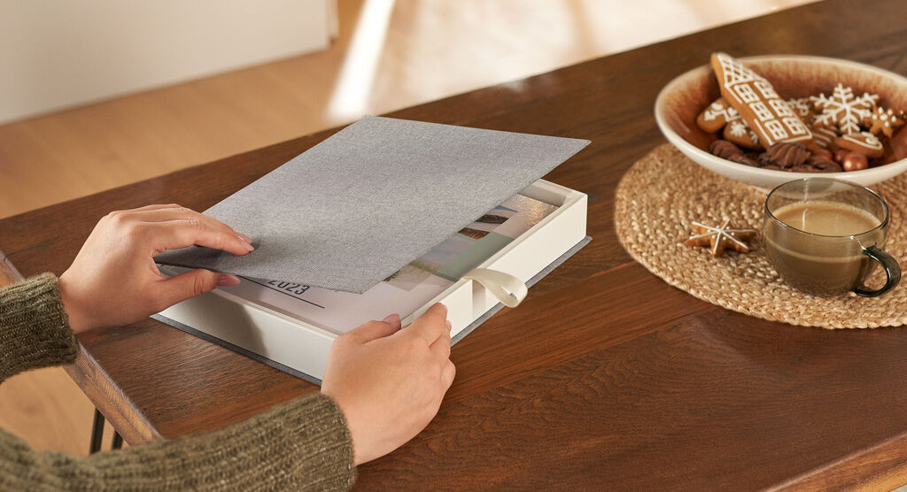 Une personne feuillette un CEWE FOTOBUCH sur une table en bois.