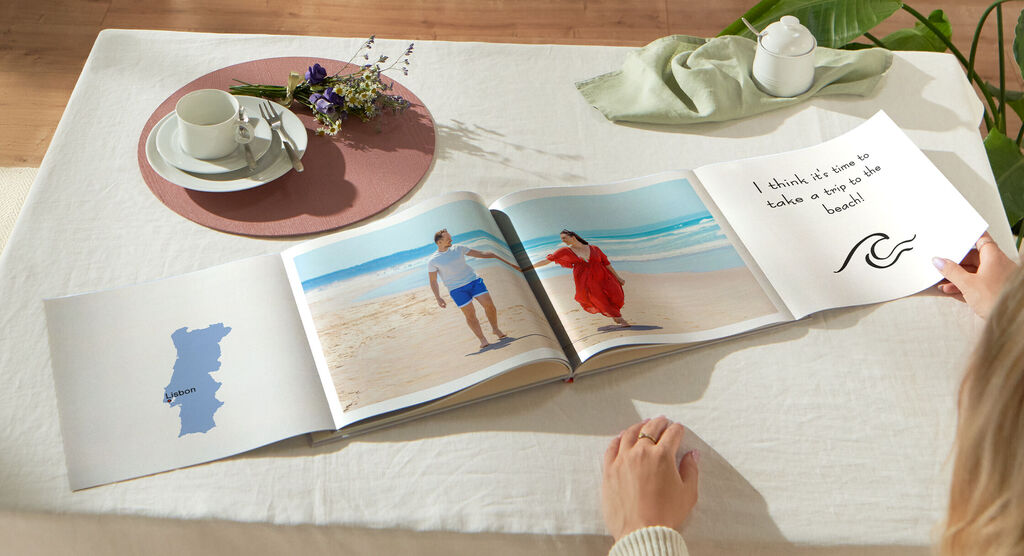 Une personne feuillette un album ouvert sur une table avec du thé et des fleurs.