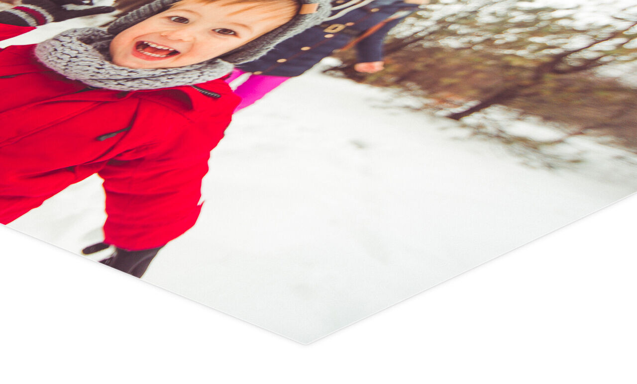 Un enfant joyeux en veste rouge et écharpe grise marche dans la neige en souriant.