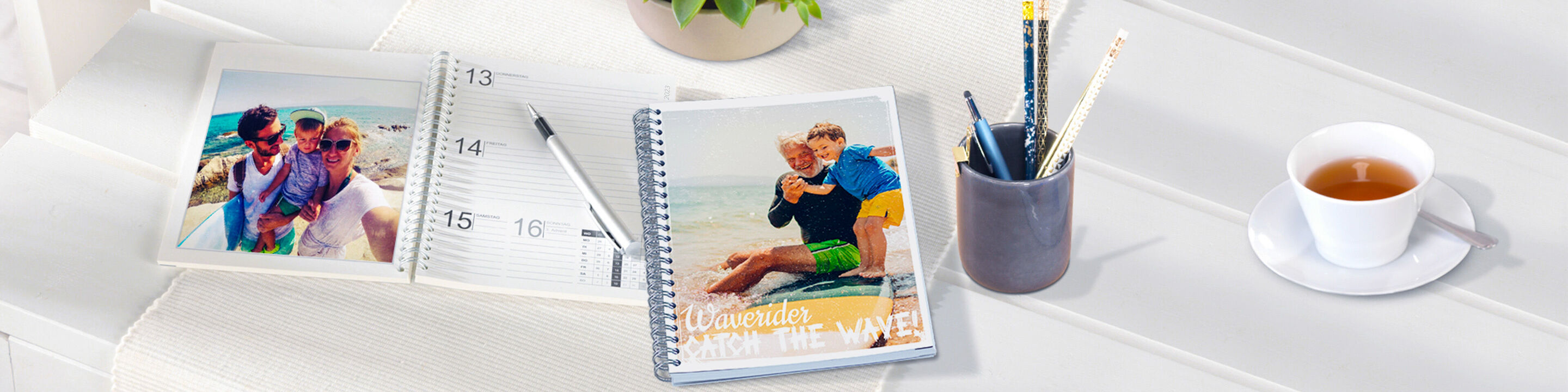 Un livre photo CEWE sur une table entouré d'un calendrier, de stylos et d'une tasse de café.
