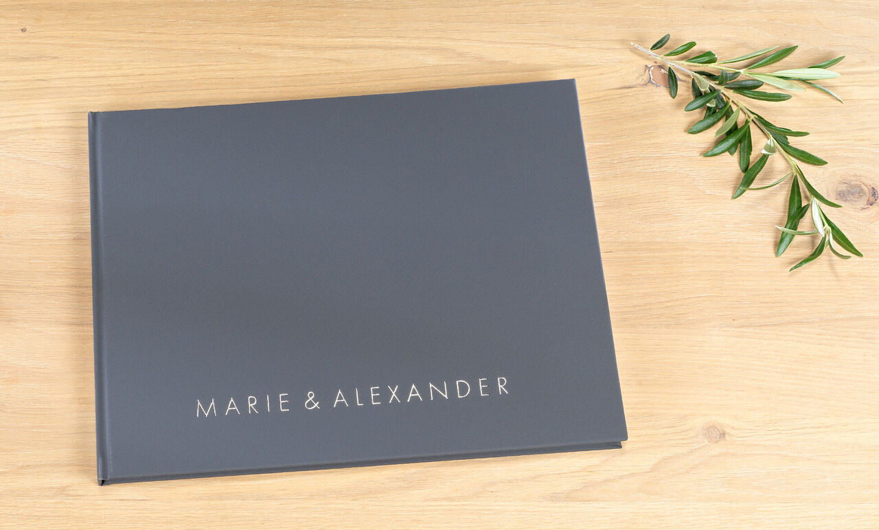 Album photo élégant et moderne avec les noms Marie et Alexander sur la couverture, placé sur une table en bois.
