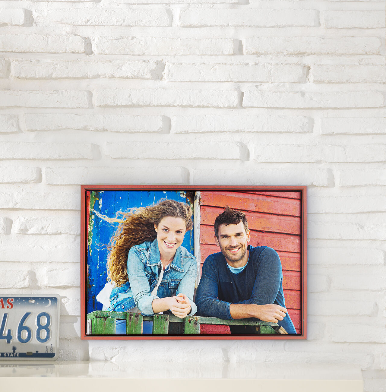 Un couple souriant s'appuie sur une clôture colorée. La femme porte une veste en jean et a des cheveux bouclés. L'arrière-plan est rouge et bleu.