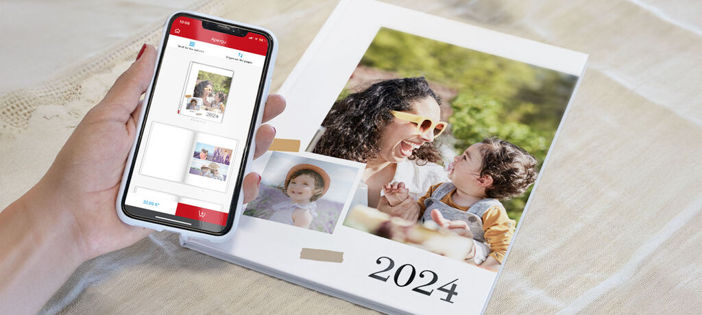 Une main tient un smartphone affichant un aperçu du CEWE Photo Book. À côté, un livre photo ouvert montrant une mère et son enfant au soleil.