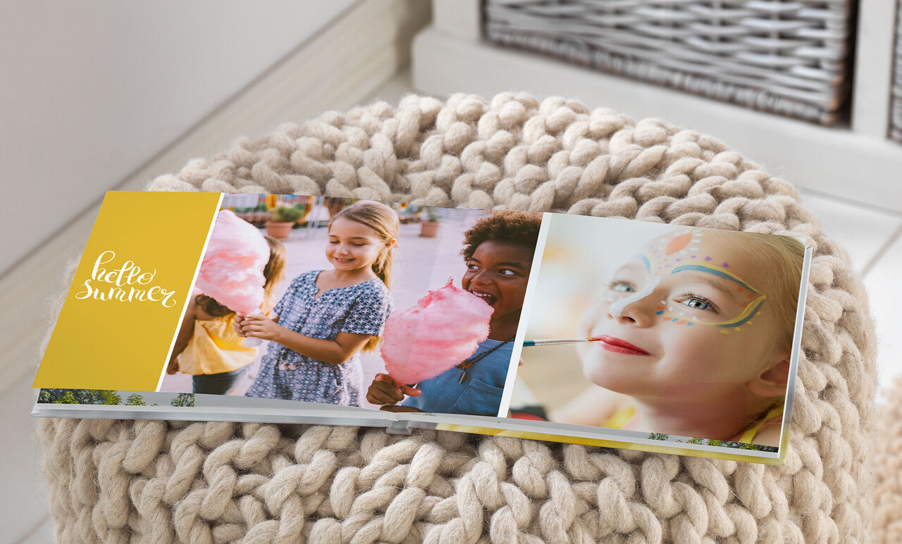 Un livre photo ouvert avec des souvenirs d'été et une page jaune montrant 'hello summer'. Il contient des photos d'enfants heureux dégustant de la barbe à papa.