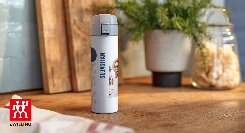Bouteille isolante avec photo de Sebastian sur une table en bois, entourée de plantes et verres
