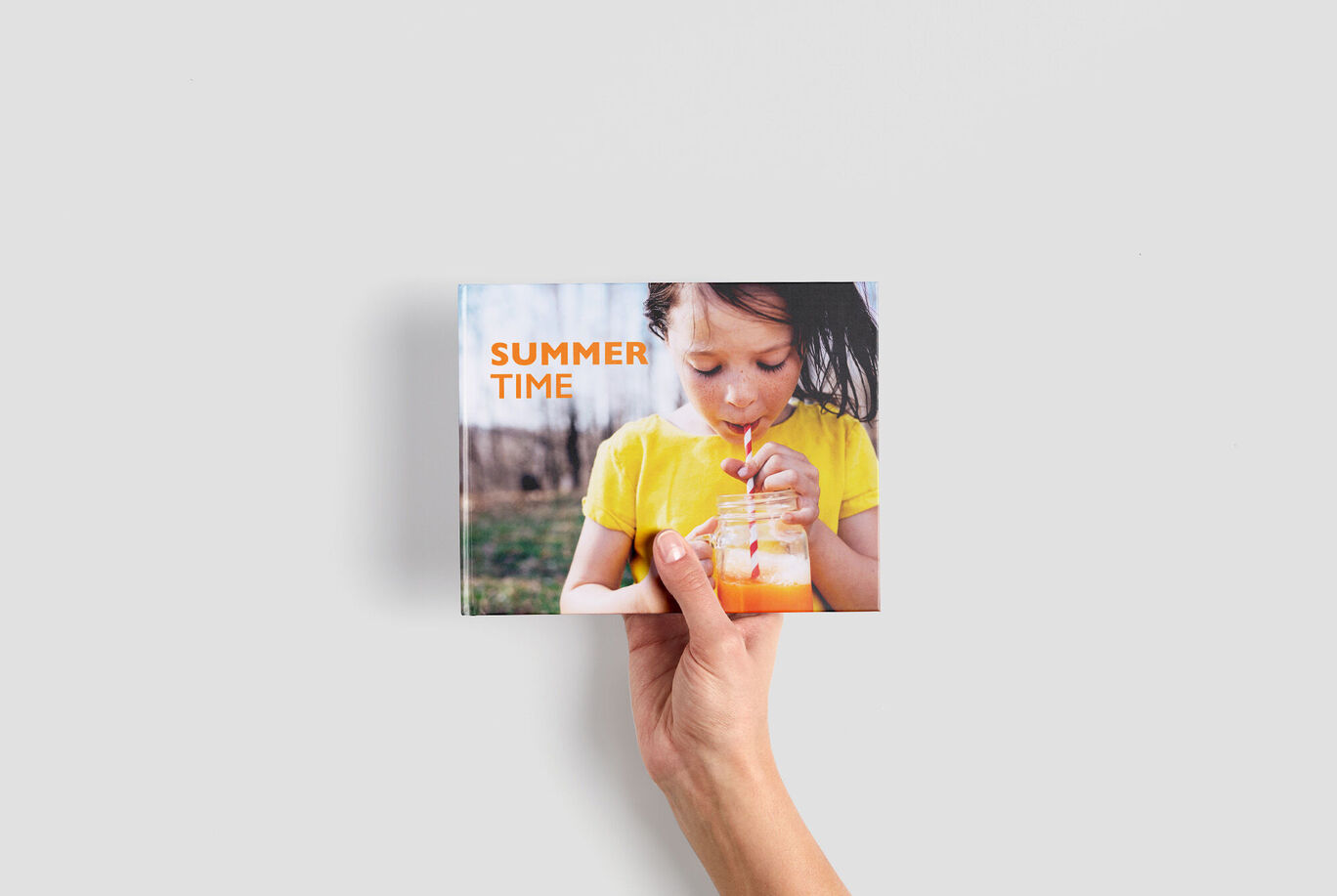 Une personne tient un livre photo CEWE avec une photo d'été joyeuse en couverture.