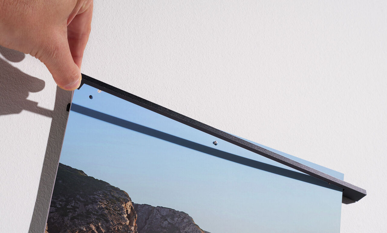 Une personne accroche un tableau CEWE au mur. Le tableau montre un paysage.