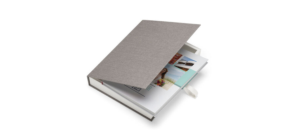 Un livre photo CEWE ouvert avec des photos colorées et une surface grise.