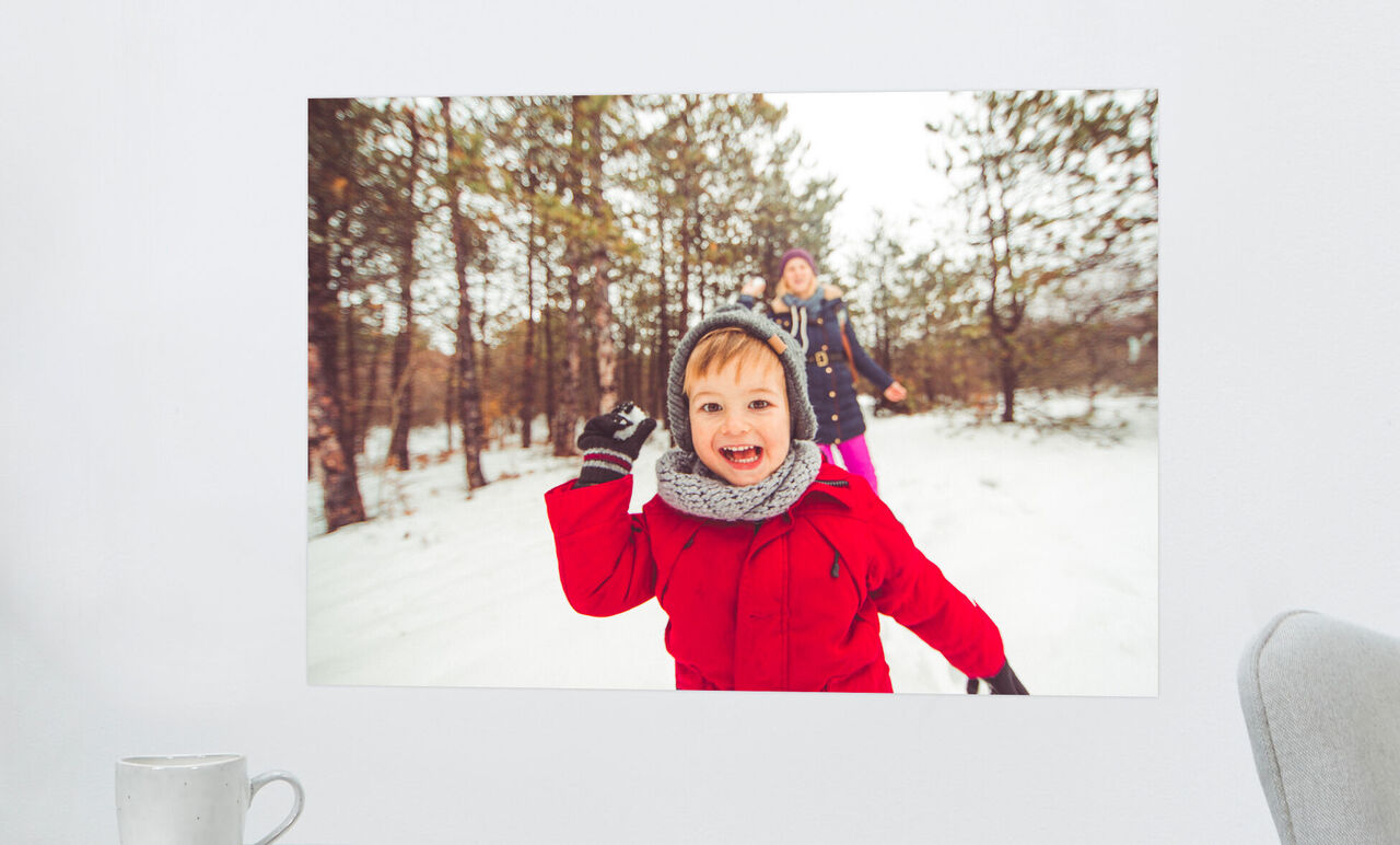 Un enfant en veste d'hiver rouge jouant joyeusement dans la neige, avec un adulte souriant en arrière-plan.