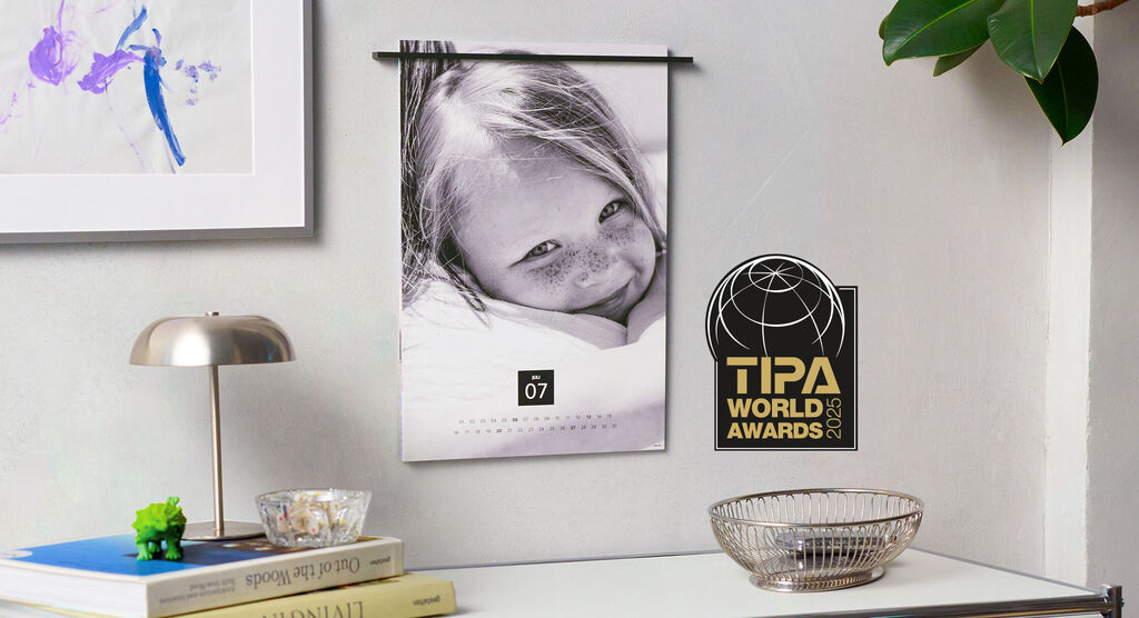 Un beau calendrier suspendu à un mur. Sur une table, une lampe, des livres et un panier.