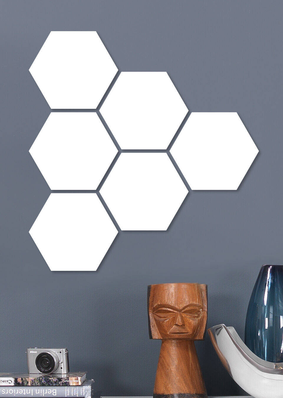 Six formes hexagonales blanches sur un mur gris, à côté d'une lampe moderne et d'une caméra
