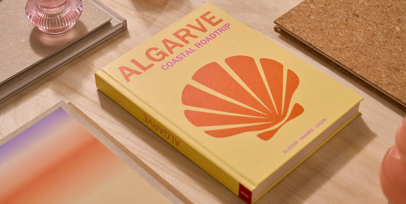 Livre photo à couverture jaune avec un coquillage orange, intitulé « ALGARVE coastal roadtrip », posé sur un bureau.