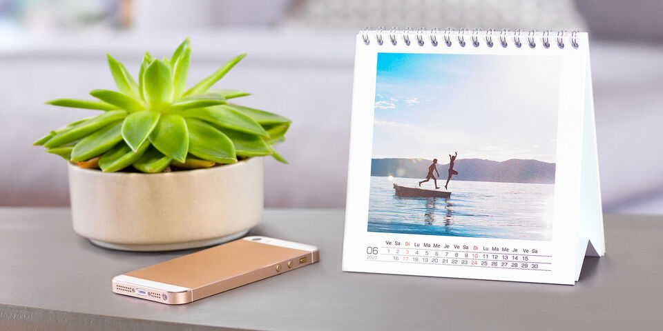 Une table avec un pot de plante verte et un calendrier CEWE, sur lequel deux personnes sont dans l'eau.